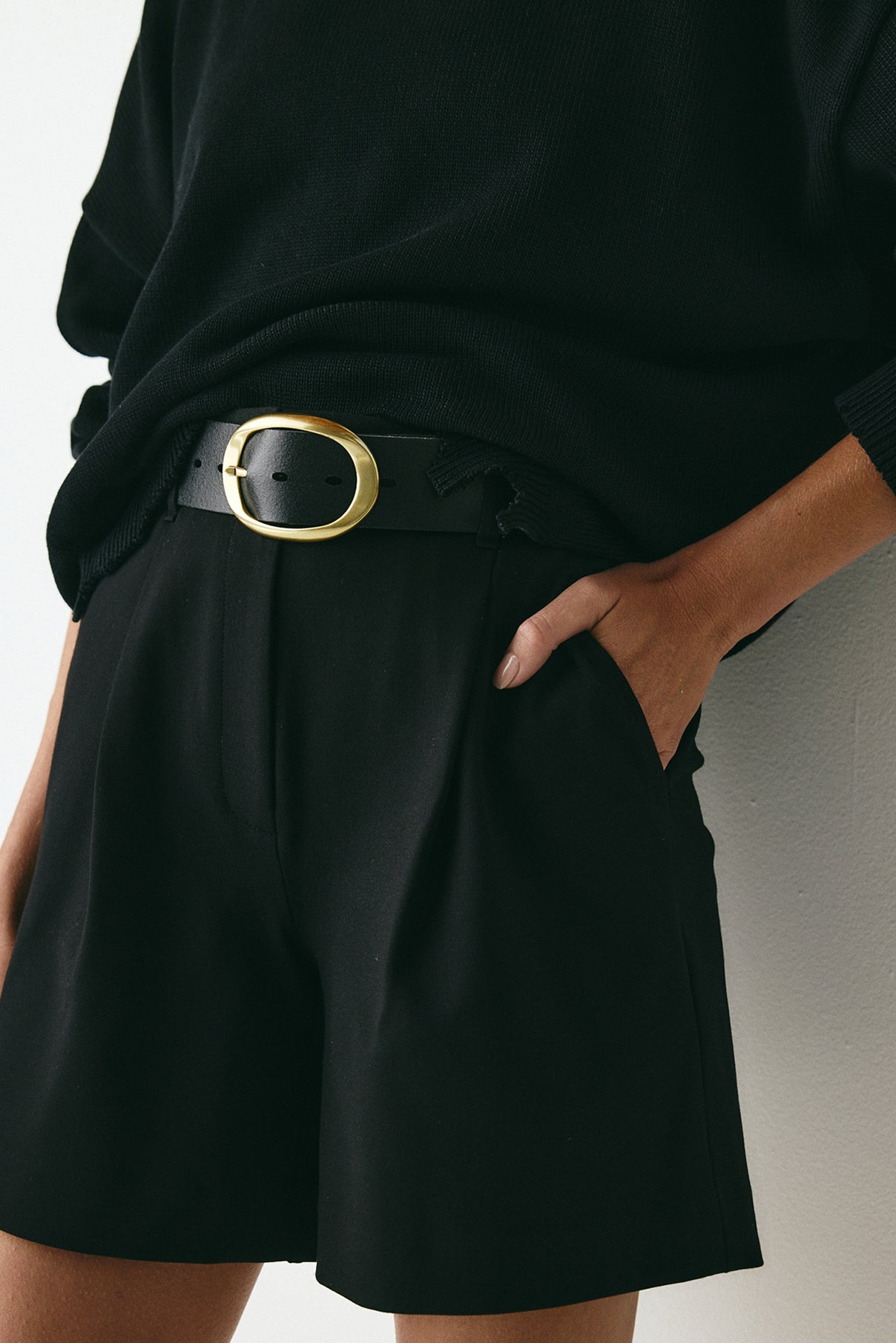 Close-up of Brooklyn black leather belt showing polished gold buckle details.