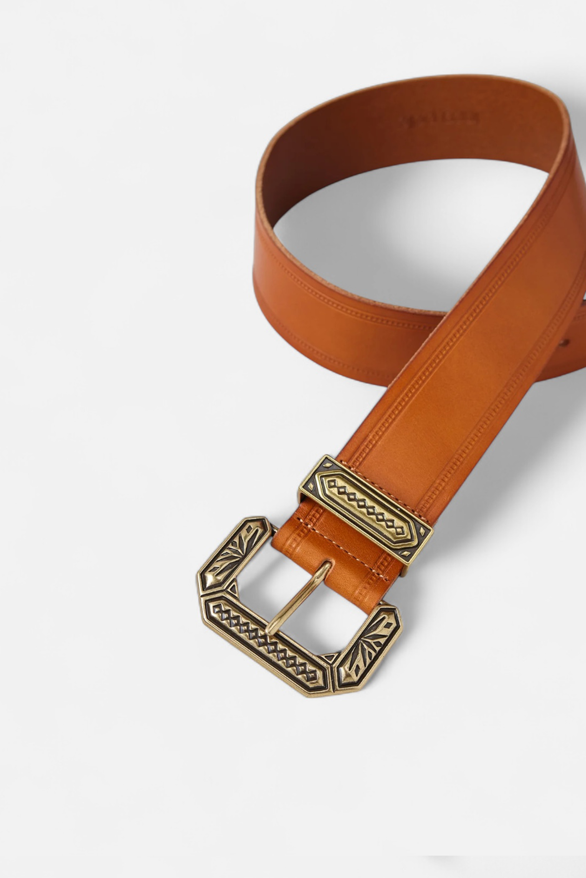 Twisted Nola vachetta leather belt highlighting engraved gold buckle and detailing.